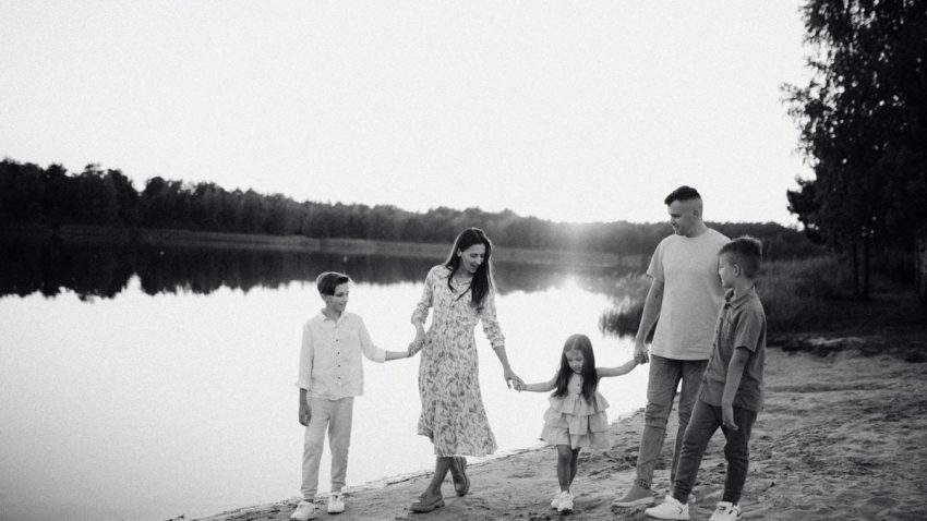 Monochrome photo of a family walking hand in hand along a serene lakeshore.